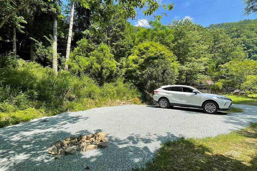 区画Bに車が停まっている画像。晴れた空の下、森の中に整地された空間がある。左手前には焚火場が見える。