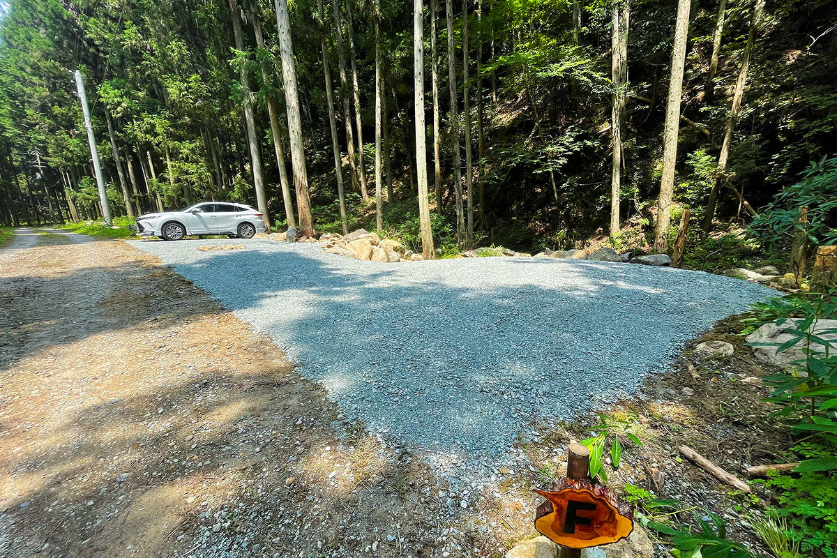 区画Fに車が停まっている画像。森の中に整地された空間がある。車の手前に焚火場が見える。