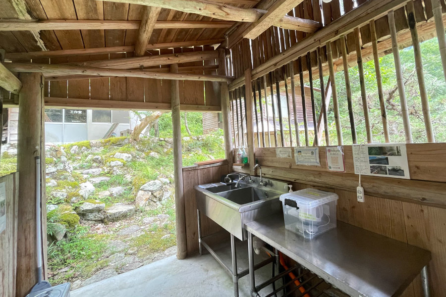 藤荘キャンプ場の共同水場。木でできた小屋の中にシンクがあり、その横に作業台がある。